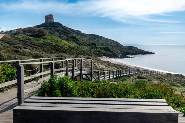 San Giovanni di Sinis - Sardinien - Italien - 03-03-2025: Uzakta San Giovanni di Sinis kulesi ve Capo San Marco ile sahile giden ahşap bir patikadan manzaralı bir manzara.