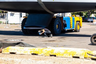 Cagliari - Sardinien - Italien - 03-10-2025: Açık güneşli bir günde tekne bir tersanede karavanda sabitlenirken bir adam omurgasına boya sürerek bir yelkenlinin altına çömeliyor.