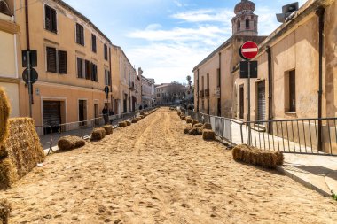 Oristano - Sardinien - Italien - 03-03-2025: Sartiglia karnavalı için hazırlanmış Oristano caddesi, açık gökyüzü altında tarihi binalar arasında kum, saman balyaları ve bariyerler kurulmuş..
