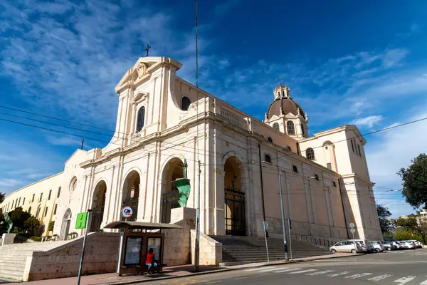 Cagliari - Sardinien - Italien - 03-11-2025: Cattedrale di Cagliari 'nin, tramvay telleri ve otobüs duraklarıyla sokaktan görülen kubbeleri, çan kulesi ve heykelleri ile barok tarzı kenar manzarası.