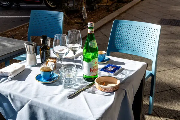 Cagliari - Sardinien - Italien - 03-11-2025: Su şişesi, kahve bardakları, şarap bardakları, kül tablası, şeker paketleri ve kaplar ile kurulmuş açık hava masası.