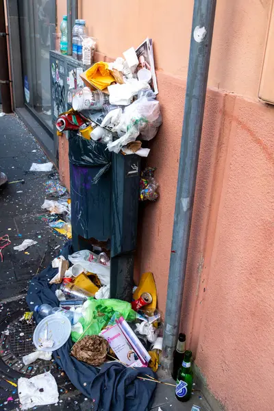 Oristano - Sardinien - Italien - 03-02-2025: Oristano 'da plastik şişeler, kağıt, yiyecek ambalajları ve kaldırıma konfetiler de dahil olmak üzere bir duvar boyunca taşan çöp tenekesi ve dağınık çöp yığını.