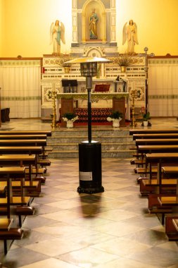 Fordongianus - Sardinien - Italien - 03-04-2025: Benzin ısıtıcısı merkezi San Pietro Apostolo kilisesi koridorunda görünür sunak, sıralar, mermer zemin ve dini heykellerle yerleştirildi.