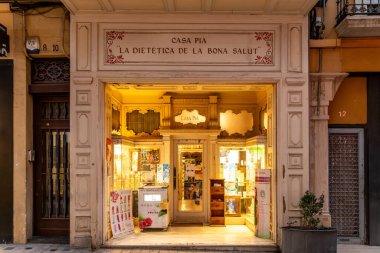 Reus, Katalonya - İspanya - 01-03-2025: Geleneksel bir sağlık ve diyet dükkanının dekoratif ahşap dekorları, cam vitrinleri ve tanıtım afişleri ile aydınlatılmış vitrinleri.