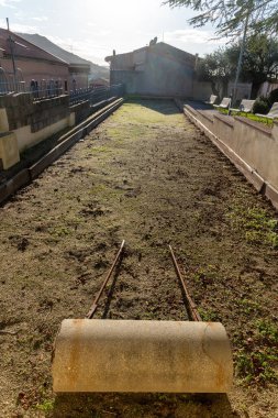 Semestene, Sardinya - İtalya - 01-12-2025: Semestene 'deki bir bocce kortunda ön planda, sıralar, duvarlar ve yemyeşil bitki örtüsüyle çevrili yıpranmış bir sarmal araç.