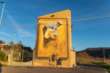 Semestene, Sardinya - İtalya - 01-26-2025: Bina duvarındaki büyük bir duvar resmi, altın buğday hasadı yapan bir çiftçiyi resmediyor..