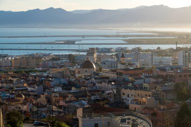 Cagliari - Sardinien - Italien - 03-11-2025: Parlak bir öğleden sonra ışığı altında renkli binalar, kilise kubbeleri, deniz limanı ve uzak dağların panoramik manzarası.