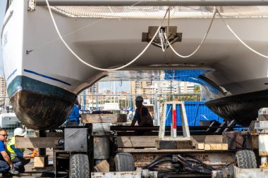 Cagliari - Sardinien - Italien - 03-14-2025: İşçiler, limanda araç ve teçhizatla vinç kaldırmaya hazırlanırken katamaranın altında duruyorlar.