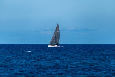 Palermo - Sizilien - Italien - 03-16-2025: Sakin sularla çevrili açık bir gökyüzü altında derin mavi denizde süzülen siyah yelkenli bir tekne.