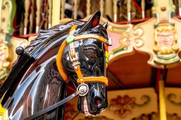 Reus, Katalonya - İspanya - 01-03-2025: Renkli aksanlı ayrıntılı dizginli parlak siyah bir atlıkarınca. Arkaplan gösterileri eski sürüşün dekorasyonlarını süsler.