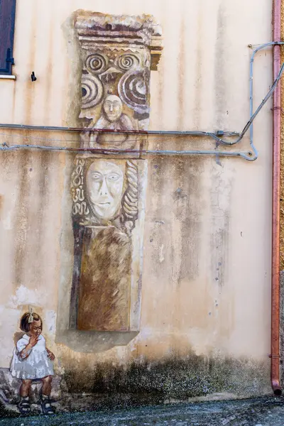 Semestene, Sardinya - İtalya - 01-12-2025: Semestene 'de antik bir taş tasarımı ve boyalı bir çocuğun yer aldığı detaylı bir duvar resmi, sanatı tarihi elementlerle harmanlıyor.