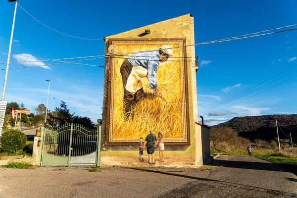 Semestene, Sardinya - İtalya - 01-12-2025: Bina duvarındaki büyük bir duvar resmi, altın buğday hasadı yapan bir çiftçiyi resmediyor..