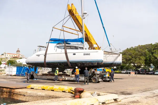 Cagliari - Sardinien - Italien - 03-14-2025: Bir katamaran sarı bir vinç tarafından sudan çıkarıldı, limanda güvenlik ekipmanları ile çevrili ve görülebilir binaları olan bir limanda.
