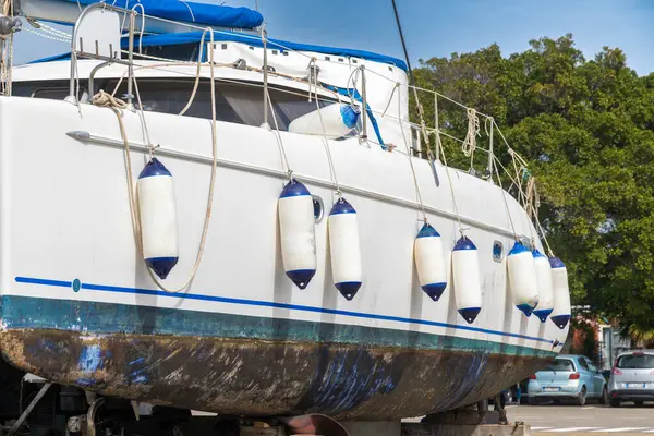 Cagliari - Sardinien - Italien - 03-14-2025: Katamaran gövdesinin yan görünüşü, arka planda ağaçlar ve park halindeki arabalarla güverte boyunca sayısız çamurluk olduğunu gösteriyor.