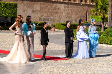 Palermo - Sizilien - Italien - 03-18-2025: Şık elbiseli beş model açık havada kırmızı halı üzerinde poz veriyor, arka planda yeşillik, güneşli bir yerde fotoğraf çekimi sırasında.