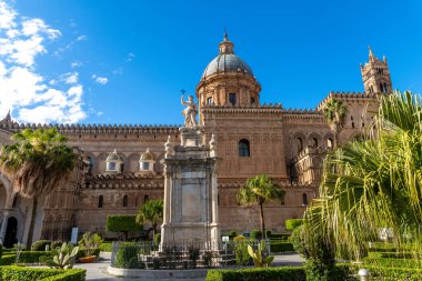 Palermo - Sizilien - Italien - 03-18-2025: Palermo Katedralleri Kubbesi ve önünde heykel olan cephe, Sicilya 'da güneşli bir günde palmiye ağaçları, kaktüsler, çitler ve mavi gökyüzü ile çevrili.