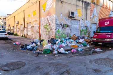 Palermo - Sizilien - Italien - 03-18-2025: Palermo 'da bir sokak köşesine yığılmış çöp yığını, duvar resimleri, park edilmiş araçlar ve çatlak kaldırıma saçılmış çöp torbaları.