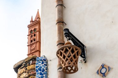 Parrini - Sizilien - Italien - 03-20-2025: Terracotta feneri ve beyaz bir duvardaki drenaj borusu, açık bir gökyüzünün altında küçük kırmızı bir çan kulesi görünür..