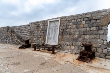 Cefalu - Sizilien - Italien - 03-24-2025: Cefalu 'daki taş liman duvarı, iki büyük paslı çapa, deniz kenarında bulutlu gökyüzü altında zincir bariyer ve merdiven.