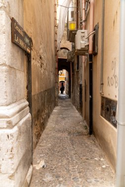 Cefalu - Sizilien - Italien - 03-24-2025: Yüksek binalar, görünür borular, duvar graffitisi, klima üniteleri ve Cefalu, Sicilya 'da arka planda yürüyen biri arasında dar patika.