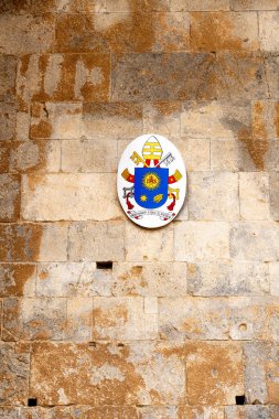 Cefalu - Sizilien - Italien - 03-24-2025: Cizvit amblemli Papalık arması, aşınmış taş bir duvara aşınma, çatlaklar ve kare deliklerle monte edilmiş çapraz anahtarlar ve Mitre.