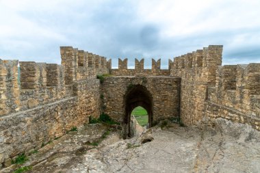Sperlinga - Sizilien - Italien - 03-25-2025: Sicilya 'daki Sperlinga Kalesi' nin taş duvarları ve güçlendirilmiş kapısı, ortaçağ siperleri ve bulutlu gökyüzünün altında bir taş patika.
