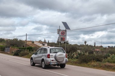 Niscemi, Sizilien - İtalya - 03-26-2025: Saatte 76 km hızla giden ve ev, bitki örtüsü ve bulutlu gökyüzü ile kaplı kırsal bir yolun kenarına monte edilmiş iki araba geçiyor.