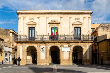 Niscemi, Sizilien - İtalya - 03-26-2025: Niscemi 'deki belediye binası kemerli giriş, balkon, İtalyan bayrakları ve neoklasik mimarisi, mavi gökyüzü ve parlak güneş ışığı altında.