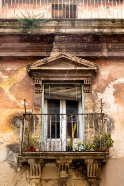 Ragusa, Sizilien - İtalya - 04-03-2025: Paslı tırabzanları, saksı bitkileri ve Sicilya 'nın Ragusa kentindeki eski bir binanın ön cephesini güpegündüz soyan eskimiş taş balkon.