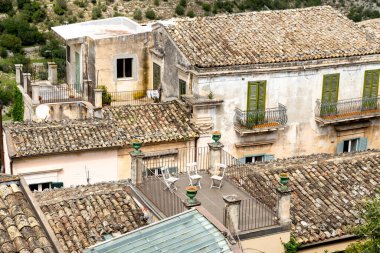 Ragusa, Sizilien - İtalya - 04-03-2025: Ragusa 'daki terasotta fayansları, yeşil panjurları ve sandalyeli bir teras, şehir mimarisinin tipik bir örneği..