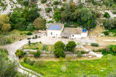 Ragusa, Sizilien - İtalya - 04-03-2025: Ragusa kırsalındaki yemyeşil, taş duvarlar ve kayalık yamaçlarla çevrili, güneş panelleri olan ıssız kırsal ev.