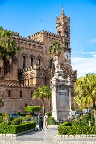 Palermo - Sizilien - Italien - 03-18-2025: Palermo Katedrallerinin önündeki heykel ve palmiye ağaçları ve ön cephe, iki kişi ve bir köpek aşağıdaki taş kaldırımlı meydanda duruyor.