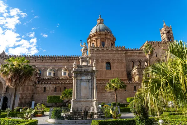 Palermo - Sizilien - Italien - 03-18-2025: Palermo Katedralleri Kubbesi ve önünde heykel olan cephe, Sicilya 'da güneşli bir günde palmiye ağaçları, kaktüsler, çitler ve mavi gökyüzü ile çevrili.