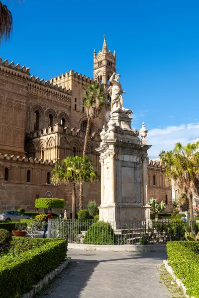 Palermo - Sizilien - Italien - 03-18-2025: Palermo Katedrali ve saat kulesi, ön planda palmiye ağaçları, çalılar ve kaldırımlı bir yürüyüş yolu bulunan büyük bir heykel yer alıyor..