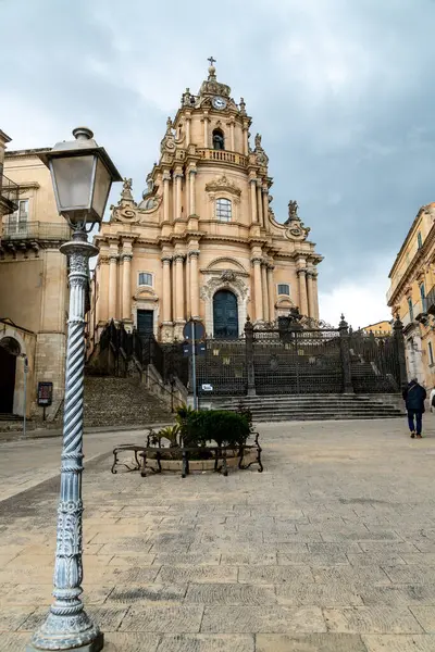Ragusa, Sizilien - İtalya - 04-03-2025: Ragusa San Giorgio Katedralleri 'nin karmaşık merdiven, demir çit ve bulutlu gökyüzünün altındaki tarihi lamba direğiyle süslenmiş görüntüsü.