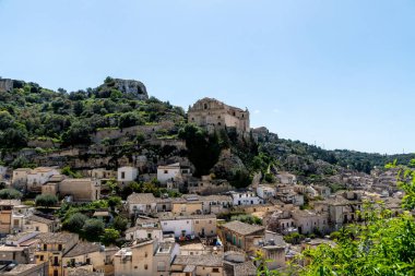 Scicli, Sizilien - İtalya - 04-05-2025: Scicli 'nin panoramik bir görüntüsü, ön plandaki evleri gösteriyor ve San Matteo Kilisesi arka plandaki bir tepenin üzerine tünedi.