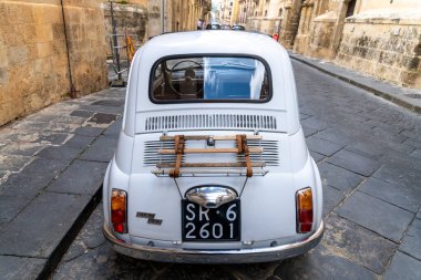 Noto, Sizilien - İtalya - 04-06-2025: Noto 'da dar bir kaldırım taşı sokakta park edilmiş klasik bir Fiat 500' ün arka görüntüsü, bagaj rafı ve klasik plaka sergileniyor.