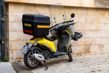 Noto, Sizilien - İtalya - 04-06-2025: Poste Italiane 'in en iyi kutusu ve ön camlı sarı scooter' ı, şehir çevresindeki bej bir duvarın yanında kaldırım taşlarının üzerine park edilmiş..