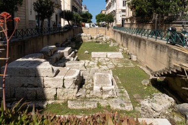 Syrakus, Sizilien - İtalya - 04-08-2025: Syracuse 'daki antik Apollo Tapınağı kalıntıları taş bloklarla çevrili, şehir binaları ve yukarıda güneşli açık bir gökyüzü.