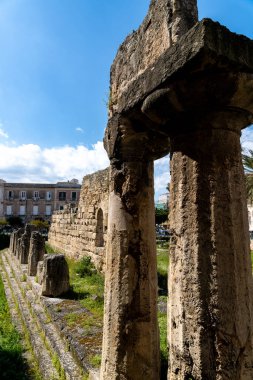 Syrakus, Sizilien - İtalya - 04-08-2025: Siraküza 'daki Apollo Tapınağı' nın parlak mavi gökyüzü ve uzak binalarıyla çevrili yıpranmış taş sütunları ve kalıntıları.