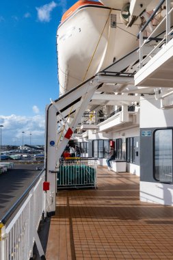 Cagliari - Sardinien - Italien - 03-15-2025: Europa Sarayı feribot güvertesi, filika, rıhtım manzaralı ve güneşli havalarda liman terminalinde mavi gökyüzünün altında oturan yolcular.