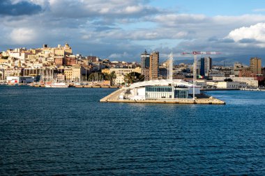 Cagliari - Sardinien - Italien - 03-15-2025: Güneşli bir günde Europa Sarayı feribotundan görülen beyaz feribot terminali, şehir binaları ve tepeleri ile Cagliari limanının manzarası.