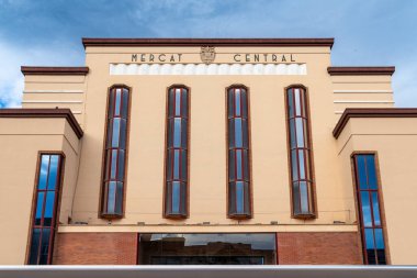 Mercat Central 'ın ön cephesinde uzun dikey pencereler ve Art Deco mimarisi yer almaktadır. Bej bina mavi gökyüzü ile çelişiyor..