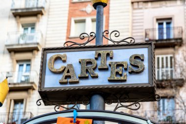 'CARTES' yazılı klasik stil tabelasının yakın çekiminde, tarihi bir binanın ön cephesine karşı kurulmuş, dekoratif metal bir çerçevede altın harflerle süslenmiş.