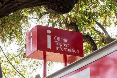 Kalın harflerle kırmızı ve beyaz bir turist bilgilendirme işareti yeşil yaprakların zeminine karşı durarak,