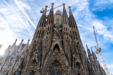 Sagrada Familia 'nın karmaşık cephesinde yüksek kuleler, ayrıntılı heykeller ve inşaat vinçleriyle ayrıntılı taş işçiliği yer alıyor.