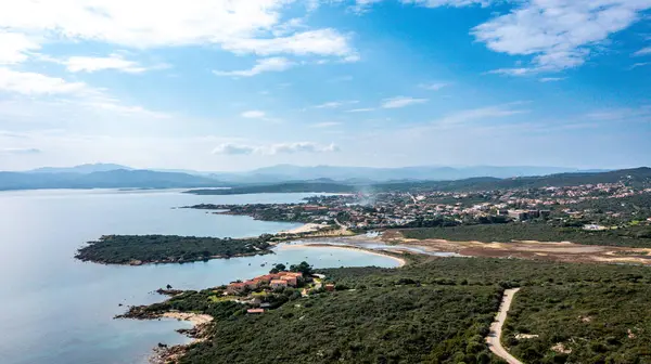 Nodu Pianu bölgesinde sakin bir günde kumsalları, koyları, tepeleri ve parçalı bulutlu gökyüzünün altındaki uzak dağları olan kıyı kasabasının havadan görünüşü.