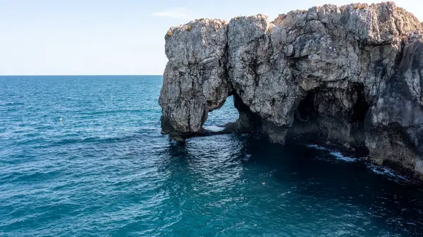 Syracuse yakınlarındaki engebeli kıyı şeridindeki devasa kaya kemeri, mavi denizden yükselen dokulu kayalıklar ve su kenarında görünen mağaralar..