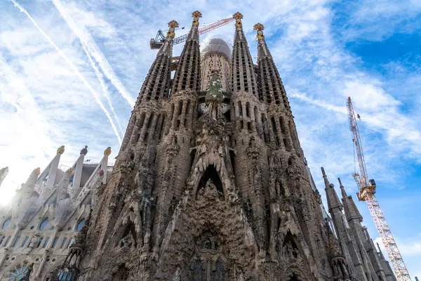 Sagrada Familia 'nın karmaşık cephesinde yüksek kuleler, ayrıntılı heykeller ve inşaat vinçleriyle ayrıntılı taş işçiliği yer alıyor.