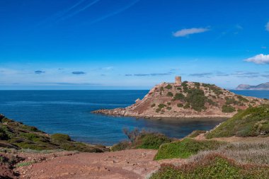 Mavi deniz, engebeli uçurumlar ve açık gökyüzünün altındaki yeşil çalılarla çevrili antik taş gözetleme kulesiyle Rocky sahil tepesi..
